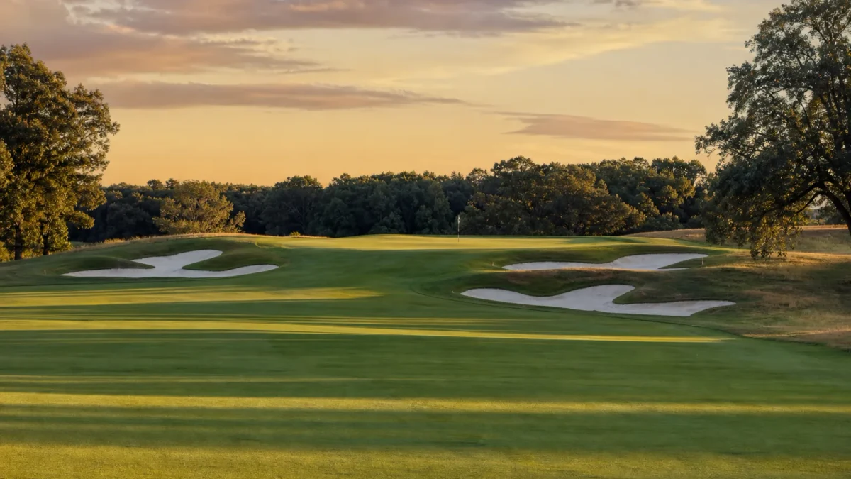 Golfbana med fairway, bunkrar och green i kvällsljus